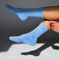Person wearing light blue socks with a brand logo on a gray background
